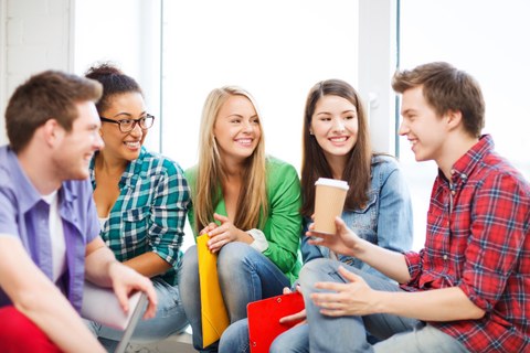 Das Foto zeigt fünf Studierende, die sich im Kreis gegenüber sitzen. Sie haben Hefter und Kaffeebecher in der Hand und lachen.
