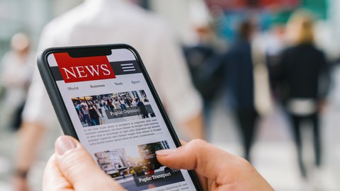 Das Foto zeigt die Hände einer Person. Sie hält ein Smartphone in der Hand, worauf Nachrichten zu erkennen sind.