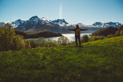 Young man with a backpack standing on the background of mountains and lake. Space for your text message or promotional content. Travel lifestyle ... 