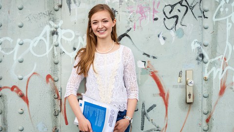 Photo: A TUD student stands smiling in front of a metal door with graffiti on the Blue Wonder.