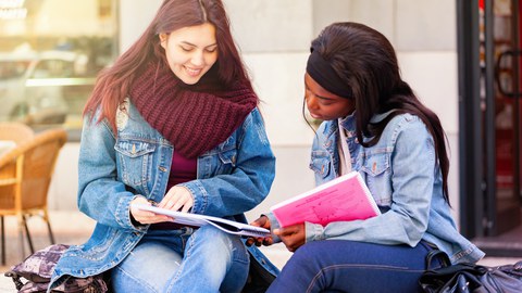 Zwei Frauen sitzen vor einem Gebäude und unterhalten sich.