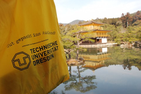 Foto eines gelben Stoffbeutels mit TUD-Logo und im Hintergrund sieht man ein japanisches Gebäude am See