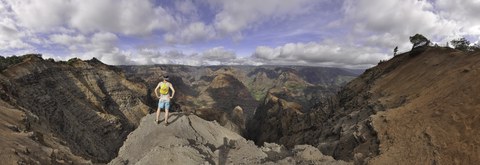 Eine Person steht auf einem Felsvorsprung und blickt in eine weitläufige, farbige Canyonlandschaft.