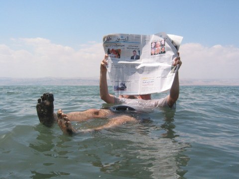 Person floating in the Dead Sea, reading a newspaper