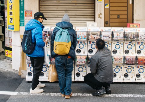 three people in front of a row of gachapon machines