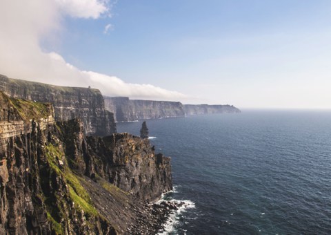 Side view of high, rugged cliffs stretching into the distance. Next to them is the blue sea.