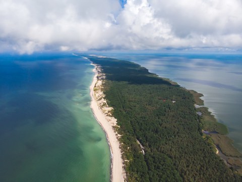 aerial view of a long spit of land in the sea, covered with forests and dunes