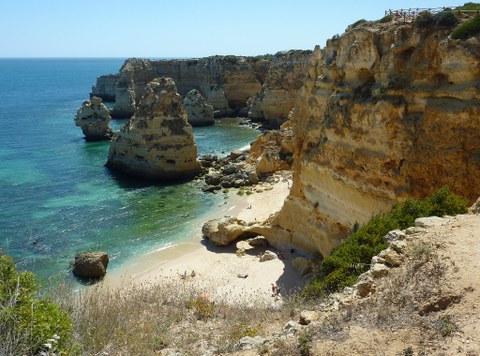 rough cliffs next to a sunny beach, a bright blue sea
