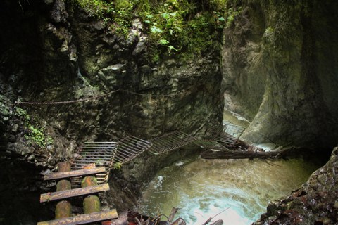 Ein Weg aus Metallstiegen führt durch eine Schlucht mit Wasserfall