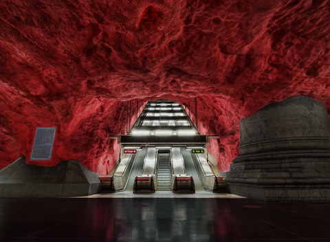 Unter einer leuchtend roten Höhlendecke beginnt eine Rolltreppe