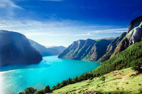 The bright turquoise waters of a fjord surrounded by mountain ranges under a deep blue sky.
