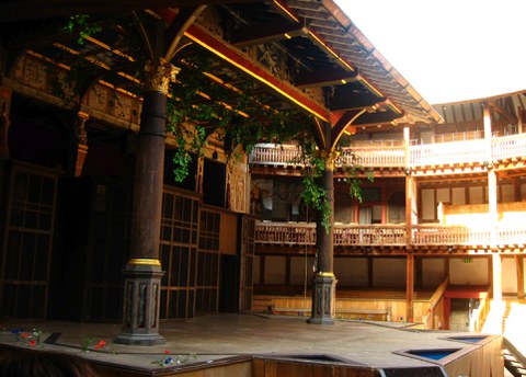 Open stage supported by two wooden pillars hung with plants. Behind, three levels of wooden galleries.