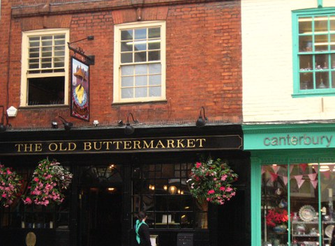 facade of a pub, with dark wooden panels, a golden name and flower pots