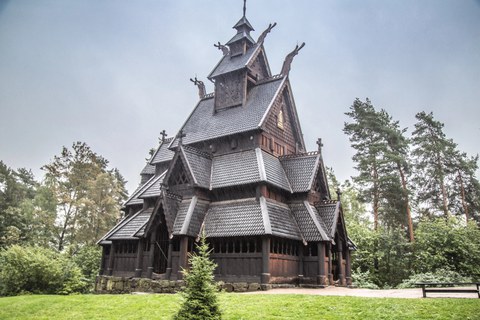 Norwegische Stabkirche, gebaut aus Holz und mit mehreren Ebenen von Dächern, deren Giebel mit Holzfiguren geschmückt sind.