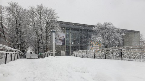 Das Foto zeigt das Hörsaalzentrum der TU Dresden und im Vordergrund die Brücke. Es schneit sehr stark und die Brücke ist völlig zugeschneit.