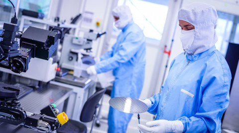 Foto von Personen in Schutzkleid in einem Labor. Eine Person hält einen Siliziumwafer in der Hand. 