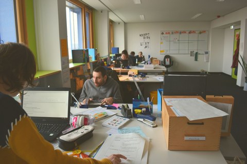 In einem Workshopraum sitzen sich Teilnehmende des Workshops an Tischen gegenüber und arbeiten an PCs.