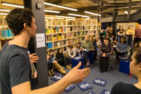 Ein Schreibtutor begrüßt eine Gruppe von circa 30 Teilnehmenden zur Langen Nacht des Schreibens in der SLUB-Zweigbibliothek Erziehungswissenschaften.