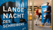 Im Foyer der SLUB-Zweigbibliothek Erziehungswissenschaft stehen zwei Roll-Up-Banner: Auf einem steht "Lange Nacht des Schreibens", auf dem anderen "Schreibzentrum". Zwei Personen laufen durch das Bild, sind aber durch ihre Laufbewegung nicht erkennbar.