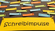 An eine Pinnwand sind viele verschiedenfarbige Zettel geheftet. Auf einem großen gelben Zettel steht "Schreibimpulse".