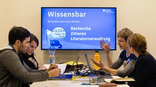 Zwei Mitarbeiterinnen der SLUB beraten zwei Studierende zu den Themen Recherche, Zitieren und Literaturverwaltung. Sie sitzen zu viert an einem Tisch, vor ihnen stehen Laptops.