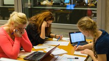 Drei Studentinnen arbeiten in einem Gruppenraum an einem Tisch, auf dem sie ihre Laptops und viele Handouts verteilt haben.