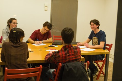 In einem Gruppenarbeitsraum tauscht sich eine Schreibgruppe in fröhlicher Atmosphäre aus. Die Teilnehmenden lächeln.