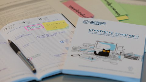 Die broschüre Starthilfe Schreiben liegt neben einem Terminkalender, in dem die Abgabe einer Bachelorarbeit rosa markiert hervorgehoben ist.