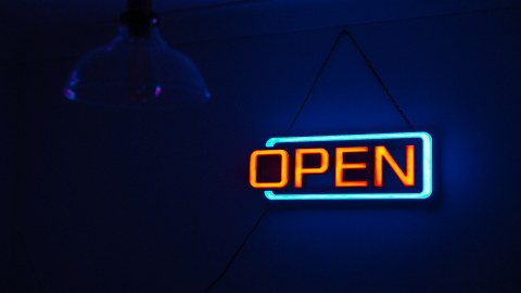 Das Foto zeigt eine Neonleuchttafel, auf der in orangefarbenen Lettern "OPEN" steht. Der Hintergrund ist dunkelblau.