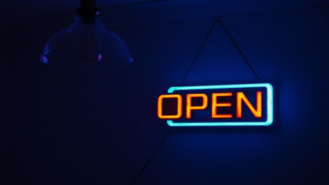 Das Foto zeigt eine Neonleuchttafel, auf der in orangefarbenen Lettern "OPEN" steht. Der Hintergrund ist dunkelblau.