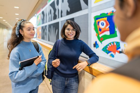 Foto von drei Studierenden an der TUD, die sich in einem bunt dekorierten Gang unterhalten.