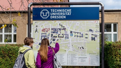 Das Foto zeigt eine Informationstafel. Auf dieser ist die Lage der einzelnen Gebäude auf dem Campus der TU Dresden dargestellt. Vor der Tafel stehen zwei Frauen. Eine zeigt mit ihrem Finger auf ein Gebäude auf der Tafel.
