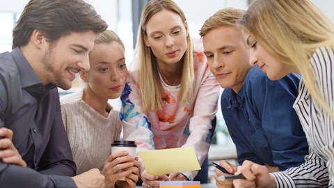 Abbildung einer Gruppe von 5 Studierenden, die sich gemeinsam einen Zettel anschauen