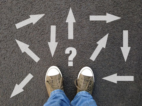 A picture of a pair of shoes standing on the ground. In front of the shoes is a questionmark and many arrows pointing at different directions.