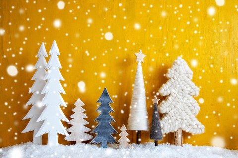 Weihnachtsdekoration aus Bäumen auf Kunstschnee vor einer gelben Wand mit Schneeflocken.