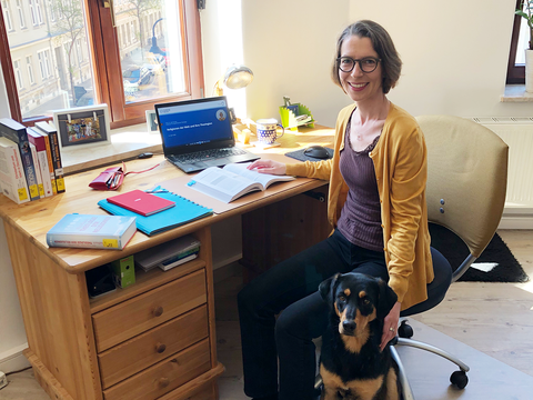 Professorin sitzt zu Hause mit ihrem Hund vor Ihrem Schreibtisch und schaut in die Kamera.