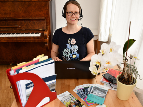 Frau sitzt mit Headset am Schreibtisch vor dem Laptop.