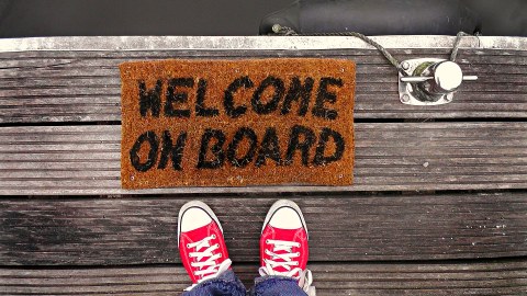 Draufsicht rote Chucks vor einer Fußmatte mit dem Schriftzug Welcome on Board