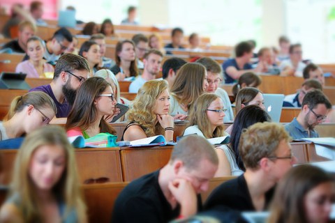 Studierende im Hörsaal hören zu und schreiben mit