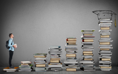Mann mit Büchern in den Händen und Rucksack auf dem Rücken steht auf der ersten Stufe einer Treppe, bestehende aus einzelnen Stapeln von Büchern, mit einem Alumni-Hut auf dem obersten Stapel