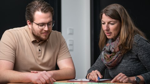 A woman and a man sit facing each other at a round table and talk. They are a student counselor and a client.