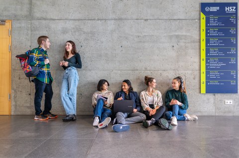 Fotos von 4 auf dem Boden sitzenden und 2 stehenden sich unterhaltende Studierenden in einem TUD-Gebäude.