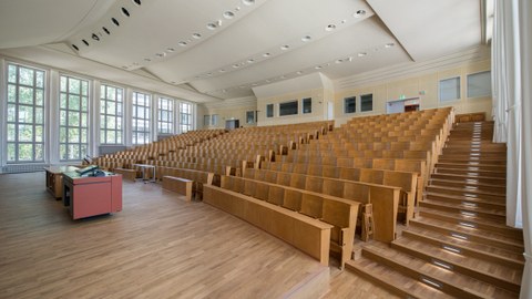 Das Foto zeigt den Schönfeld-Hörsaal auf dem Campus der TU Dresden. Man sieht die leeren Bankreihen und am linken Bildrand das Rednerpult.