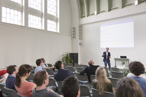 Eine Lehrperson vor einem Auditorium von ca. 12 Personen.