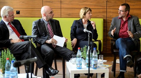 Das Foto zeigt vier Personen in Businesskleidung bei einer Diskussionsrunde.