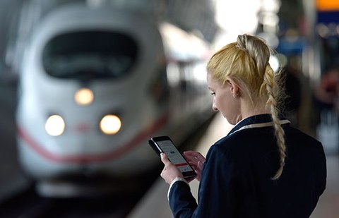 The photo shows a woman looking at her phone. A Deutsche Bahn intercity express train can be made out in the background.