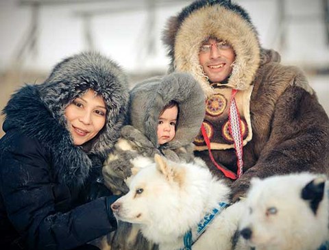 Das Foto zeigt einen Mann, eine Frau und ein Kind, die sehr dicke Jacken tragen. Davor erkennt man zwei Hunde.