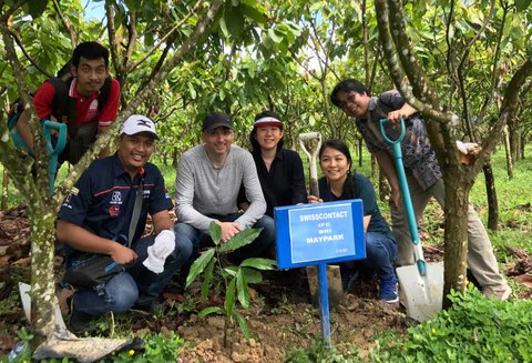 The photo shows a group of people, including Dirk Lebe. Some of them have a spade in their hands. They are crouched below a cacao tree.