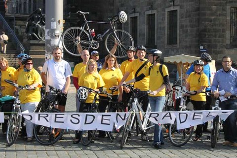 Das Foto zeigt viele Personen in gelben T-Shirts mit Fahrrädern. Im Vordergrund erkennt man ein Banner mit der Aufschrift "Dresden radelt".