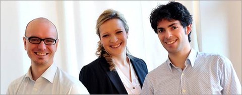 The photo shows three people dressed in businesswear smiling at the camera.